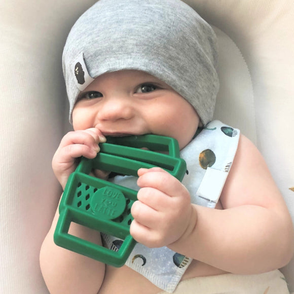 A baby in a grey hat chewing on the Itzy Ritzy latte Chew Crew. The latte is green silicone with cutouts and says, "Love You Latte".