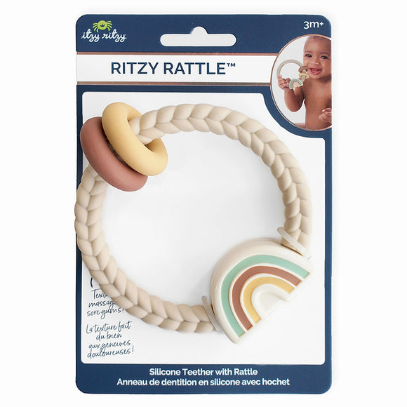 Itzy Ritzy Ritzy Rattle packaging. The package is blue and says, "Ritzy Rattle" with an image of a baby holding the tan ring with a rainbow. The product is a tan braided ring with smaller yellow and rust brown rings and a teal, rust brown, and yellow rainbow. Along the bottom, it says, "Silicone Teether with Rattle."