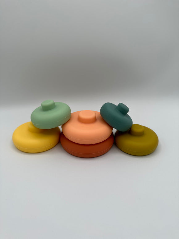 The pieces of the OB Designs Tower Stacker laid out randomly. From left to right, there is a yellow piece with a mint green piece on top of it, a red piece with a light pink piece on top of it, and an olive green piece with a teal piece on top of it.