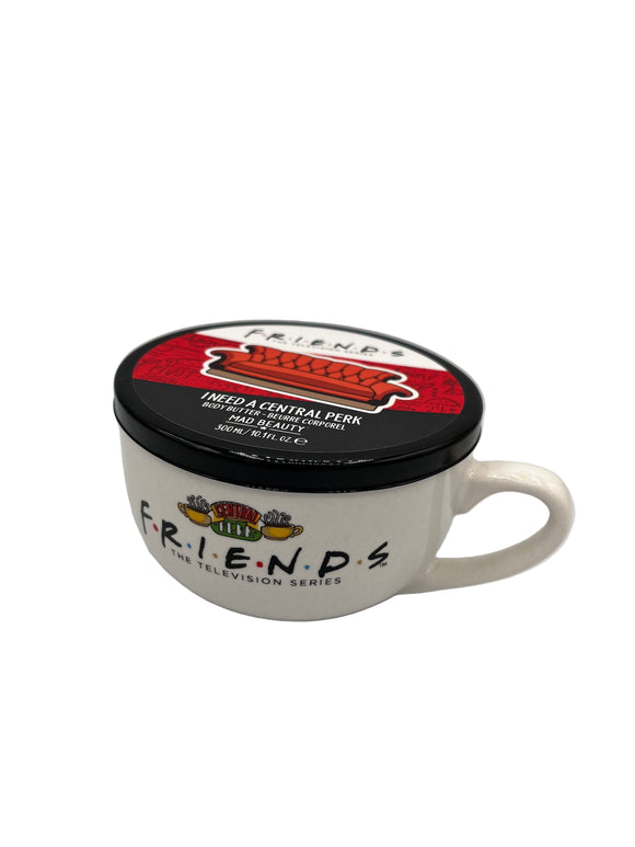 White mug shaped container that says, "friends, The Television Series" in black. Above the writing, there is an image of two yellow steaming coffee mugs outside of a green, yellow, and red sign that says, "central perk". The lid has one white stripe that says, "friends, the television series" in black, a red stripe with a red couch, and a black stripe that says, "I need a central perk, body butter - beurre corporel, Mad Beauty, 300 mL/10.1 fl oz."