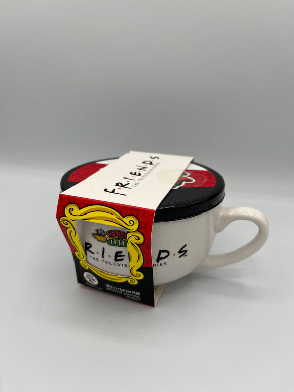 White, mug shaped container that says, "Friends, the television series" in black. Above the writing, there is an image of two steaming yellow coffee mugs surrounding a green, yellow, and red sign that says, "Central Perk". The container has a black lid with a white, red, and black stripe. Around the container, there is a paper label. The top is white and says, "Friends, the television series" in black. The front is half red and half black with a yellow frame cutout that shows the writing on the container.