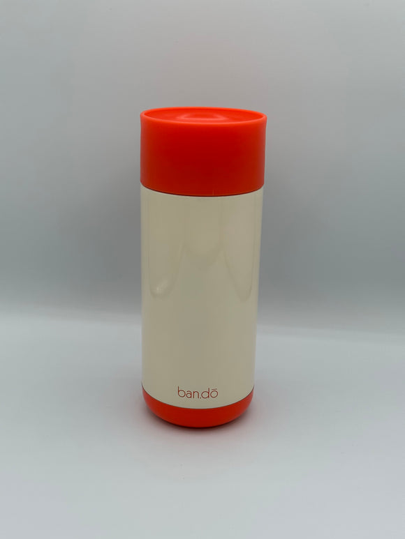 The back of the Ban-do Bold Move mug. It is cream with a red lid and red bottom and says 'ban-do' in small, thin, red letters at the bottom.