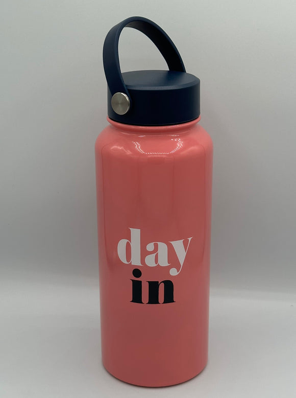 Pink metal water bottle with a navy blue lid with a carrying strap. The water bottle says, "day in" with day in white and in in navy blue.
