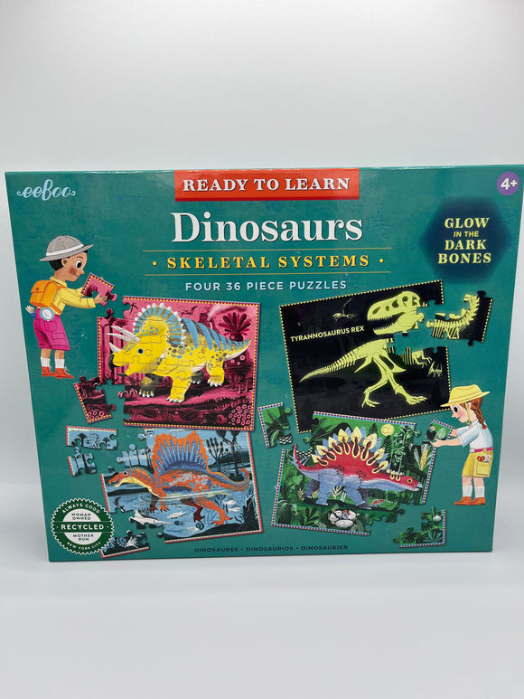 The front of the Eeboo Skeletal Systems Puzzle box. It is a teal box that says, "Dinosaurs, Skeletal Systems, Four 36 Piece Puzzles," and has a circle in the top right corner that says, "Glow in the dark bones". It showcases each of the 4 puzzles being built. Each one has a different colored background with a different type of dinosaur on it.