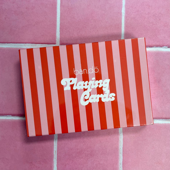 The Ban-do playing cards box. It has pink and red vertical stripes with white writing that says, "ban-do playing cards"