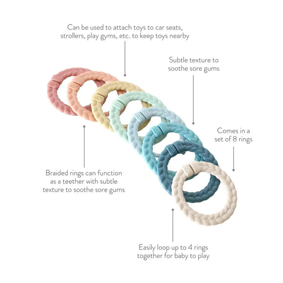 8 rainbow braided rings. From right to left, there is a blush ring, orange ring, mustard yellow, mint green, light blue, teal, dark blue, and tan. There are 5 blurbs that say, "Can be used to attach toys to car seats, strollers, play gyms, etc. to keep toys nearby," "Braided rings can function as a teether with subtle texture to soothe sore gums," "Comes in a set of 8 rings," and, "Easily loop up to 4 rings together for baby to play."