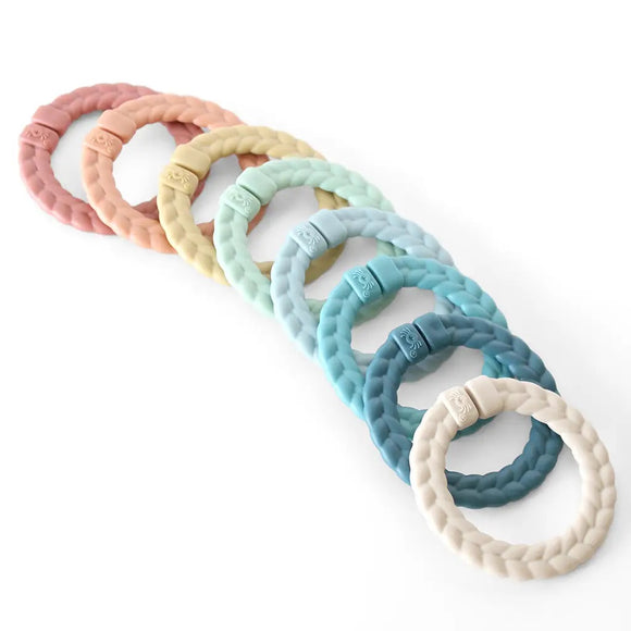 8 rainbow braided rings. From right to left, there is a blush ring, orange ring, mustard yellow, mint green, light blue, teal, dark blue, and tan.