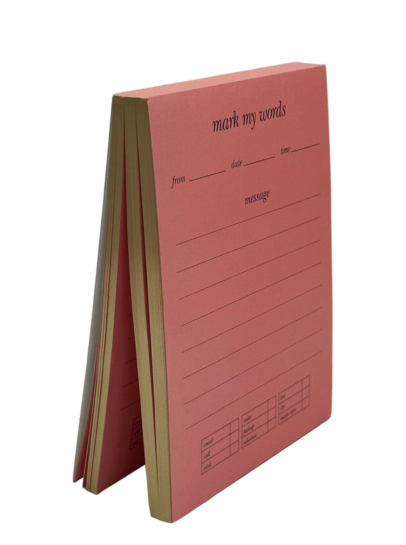 Kate Spade Mark My Words notepad. The notepad is pink with gold edges. The pages says, "mark my words, from, date,time, message" and under 'message' there are lines to write. At the bottom there are 3 charts. One says, "email, call, visit," one says, "order, pickup, schedule," and the other says, "text, dm, maybe later."