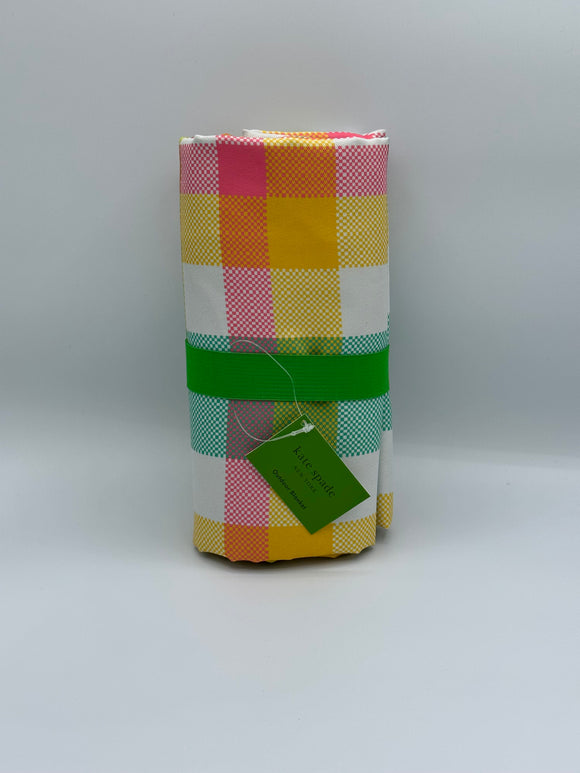 Pink, yellow, teal, and green plaid blanket rolled up with a green elastic around it and a green tag that says, "kate spade, New York, Outdoor Blanket."