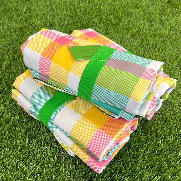 Three pink, yellow, teal, and green plaid blankets stacked on top of each other sitting in grass.