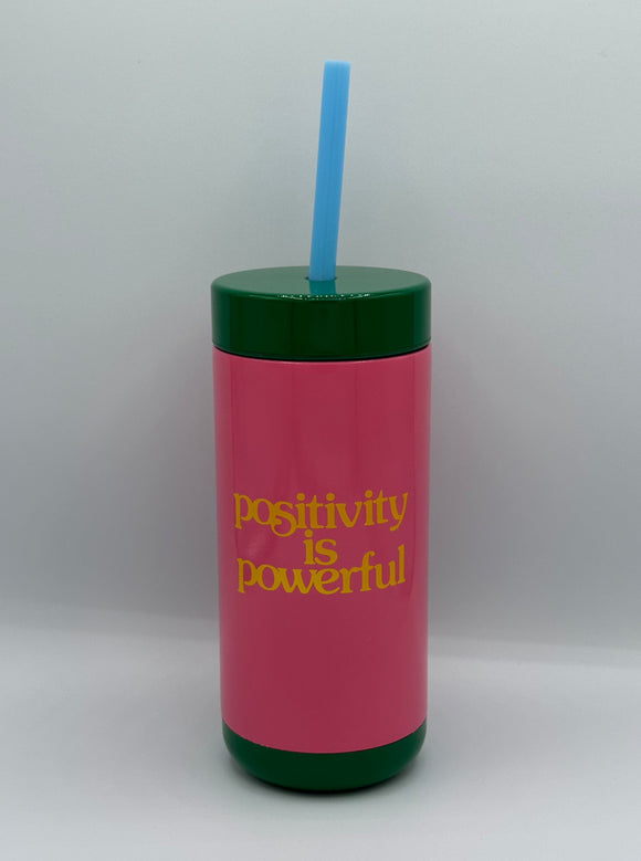 The Ban-do Positivity Tumbler. It is pink with a green top and green bottom, yellow writing that says, "positivity is powerful", and a blue straw.