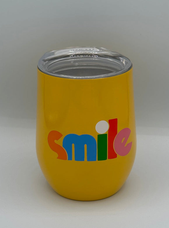 The Ban-do Smile Wine Tumbler. It is shaped like a wine glass with a clear lid. It is yellow and says 'smile' in orange, blue, green, red, and pink letters.