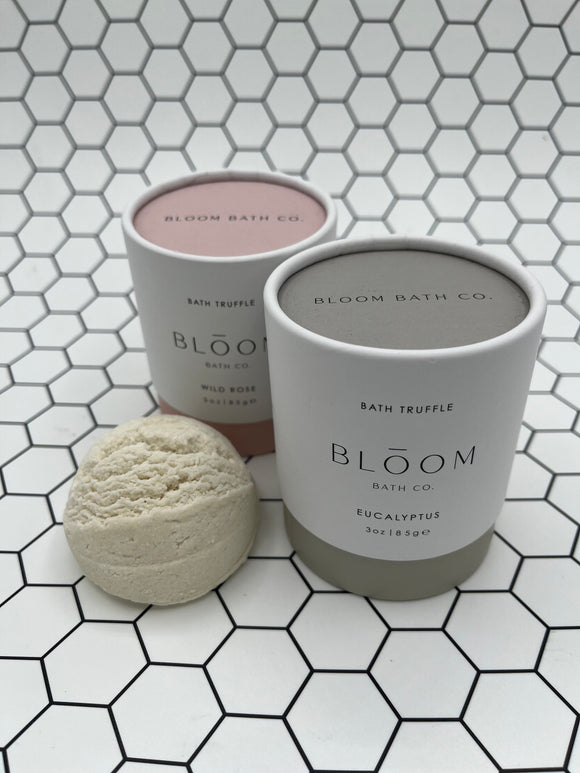 Both of the Bloom bath truffles (eucalyptus and wild rose). The wild rose tube is pink and the eucalyptus tube is sage green. There is a bath truffle featured outside of the tube in the front.