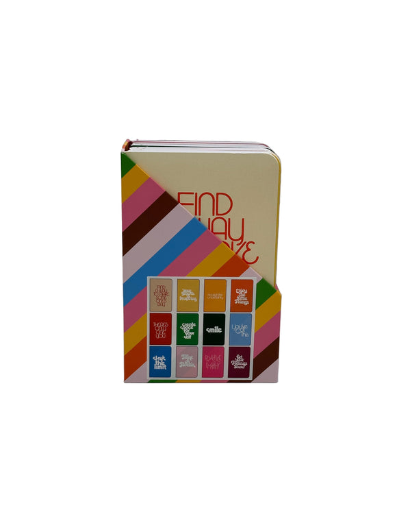 The Ban-do Wellness Notebook set. Shows them in the box they come in which has green, yellow, pink, brown, blue, and red diagonal stripes on it with an image showing each of the 12 notebooks.