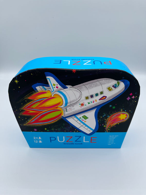 The rocket Crocodile Creek 12 piece puzzle. The box is light blue, and the front is navy blue with a rocket ship on the front.