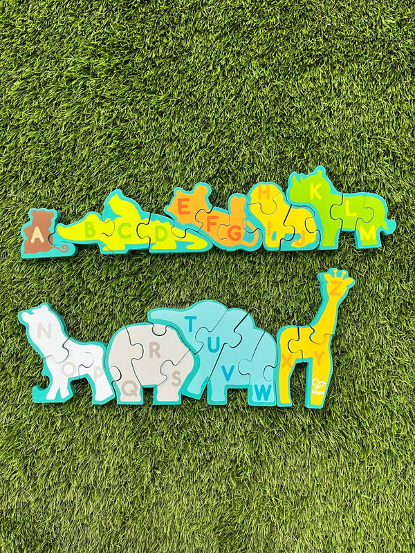 Back of the Hape alphabet and animal parade. The animals all form a line, but they are split into two. They each have different letters on the back to create the whole alphabet in order when the pieces are connected. From left to right, there is a brown monkey with an a, a yellow alligator with a b,c,d, an orange tiger with e, f, g, a yellow lion with h, i, j, a green rhino wiht k, l, m, a grey zebra with n, o, p, a grey hippo with q, r, s, blue elephant with t, u, v, w, and a yellow giraffe with x, y, z.