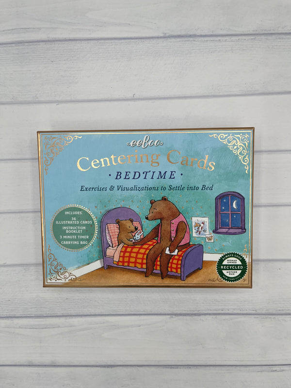 a light blue box with a gold border. It says, "eeboo Centering Cards Bedtime Exercises & Visualizations to Settle into Bed". It features a big bear tucking a little bear into bed.