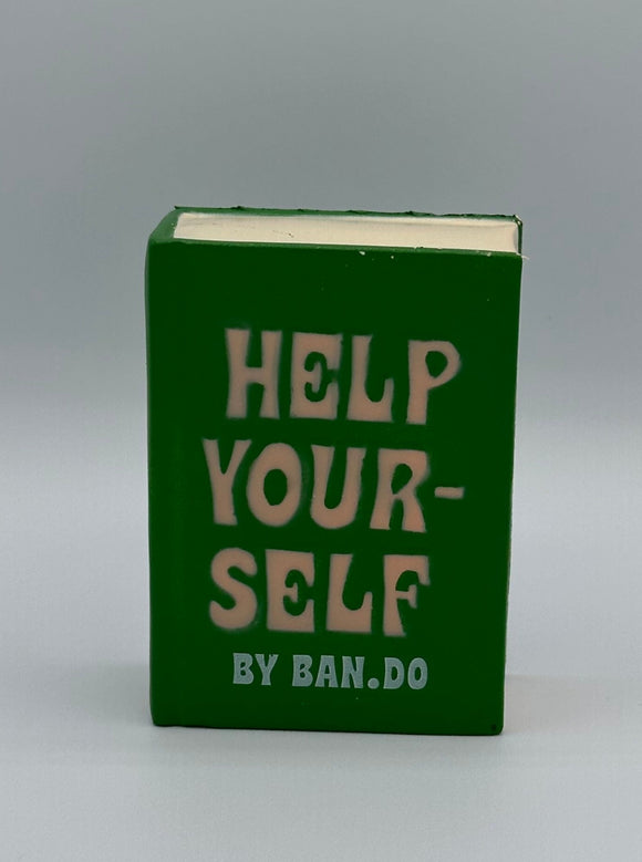 The front of the Ban-do Help Yourself De-Stress Ball. It is shaped like a book with a green cover that says, "Help yourself by Ban-do" in white writing with with pages.