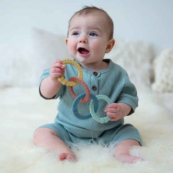 A baby holding the mustard ring, blush ring, blue ring, and mint green ring all connected.