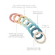 8 rainbow braided rings. From right to left, there is a blush ring, orange ring, mustard yellow, mint green, light blue, teal, dark blue, and tan. There are 5 blurbs that say, "Can be used to attach toys to car seats, strollers, play gyms, etc. to keep toys nearby," "Braided rings can function as a teether with subtle texture to soothe sore gums," "Comes in a set of 8 rings," and, "Easily loop up to 4 rings together for baby to play."