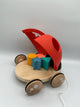 Back of the Hape Shape Sorter Ladybug. There is a wooden platform with 4 wooden wheels. On the platform there is a 3d yellow circle, orange square, blue star, and green triangle. The red wings to the ladybug are open facing upward. There is a white string to pull the ladybug.