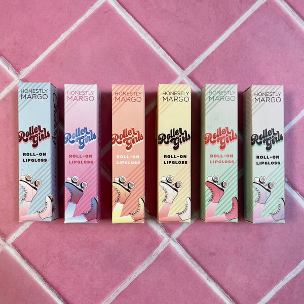 All 6 of the Honestly Margo Roller Girls Lip Glosses. (From left to right) There is a light blue box, a pink ombre box, a peach box, a light yellow box, a mint green box, and a lighter mint green box. Each box says, "Roller Girls, Roll-on Lipgloss" with roller skates on the bottom.