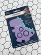 Purple dinosaur Itzy Pop in the packaging. The package is blue and says, "Itzy Pop". In the top right corner there is an image of a baby holding the teal dinosaur Itzy Pop. The product is a purple dinosaur with teal spikes and 3 popping bubbles in the middle. Along the bottom, it says, "Silicone Teether with Sensory Popper."