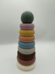 The rustic Mushie Stacking Rings tower. There are 7 rings of descending sizes going up to a ball on the top. The rings (from bottom to top) are white, dusty pink, brown, light grey, light blue, peach, yellow, and light purple with a sage green ball on top.